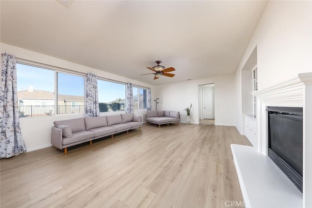 living room featuring light wood-style flooring, baseboards, a ceiling fan, and a glass covered fireplace