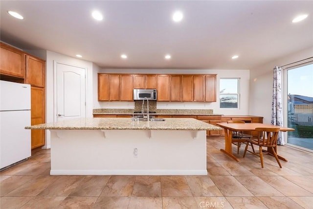 kitchen featuring recessed lighting, a kitchen island with sink, stainless steel microwave, and freestanding refrigerator