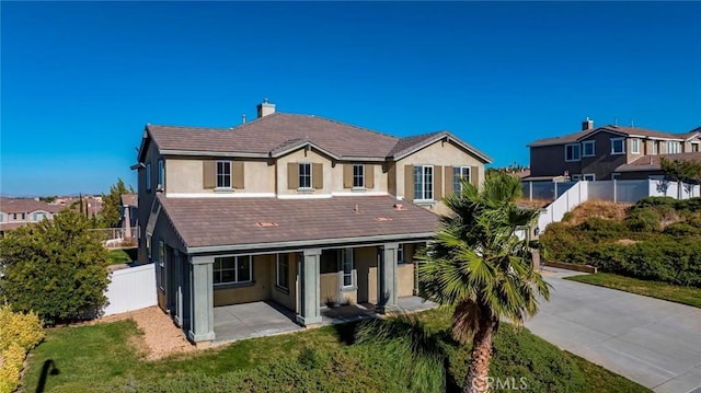 view of front of home with a chimney, stucco siding, a front yard, a patio area, and fence