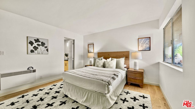 bedroom with radiator, ensuite bath, and light hardwood / wood-style flooring