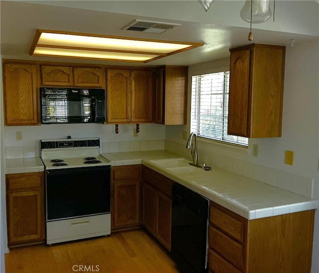 kitchen featuring sink, tile counters, light hardwood / wood-style floors, and black appliances