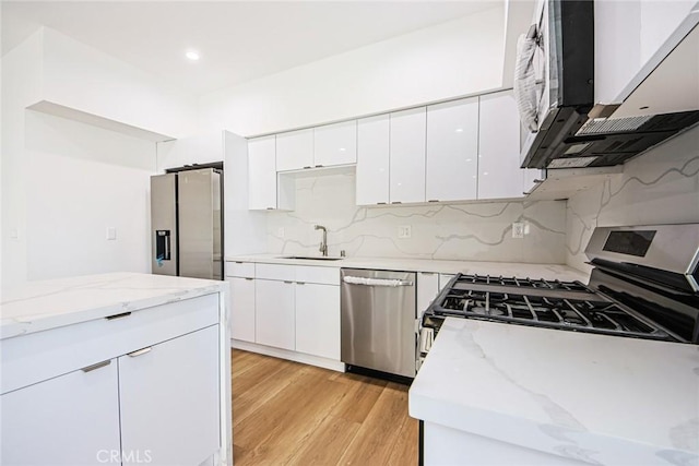 kitchen with white cabinetry, appliances with stainless steel finishes, sink, and light stone counters