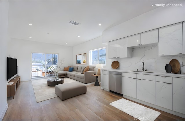 kitchen featuring tasteful backsplash, white cabinetry, dishwasher, sink, and light wood-type flooring