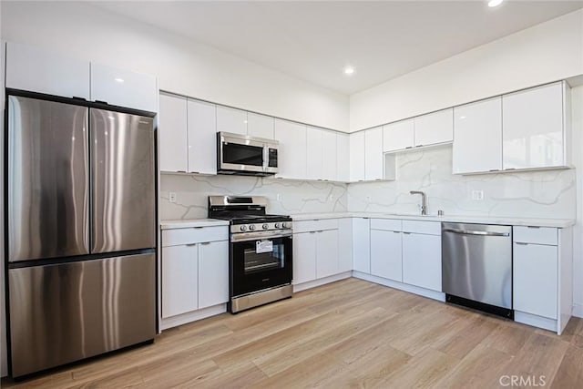 kitchen featuring sink, white cabinetry, backsplash, stainless steel appliances, and light hardwood / wood-style floors