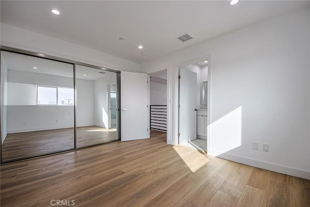 unfurnished bedroom with ensuite bath, light hardwood / wood-style flooring, and a closet