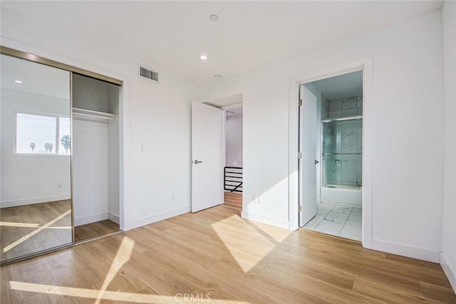 unfurnished bedroom featuring ensuite bathroom, light hardwood / wood-style floors, and a closet