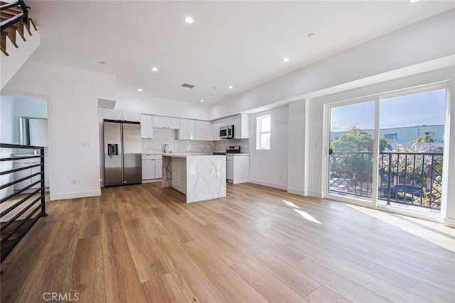 kitchen with appliances with stainless steel finishes, white cabinetry, backsplash, a kitchen island, and light wood-type flooring