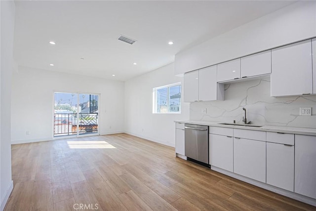 kitchen with white cabinetry, sink, backsplash, stainless steel dishwasher, and light hardwood / wood-style floors