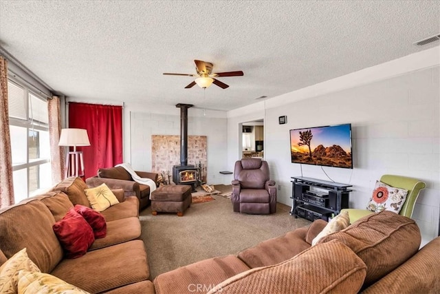 living room featuring carpet flooring, a textured ceiling, ceiling fan, and a wood stove