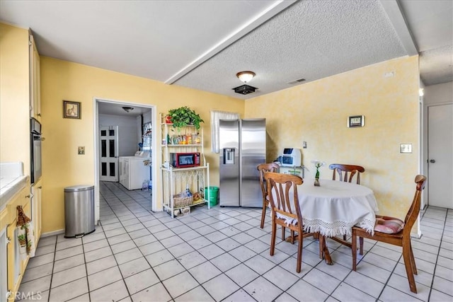 dining room featuring washing machine and dryer, light tile patterned floors, and a textured ceiling