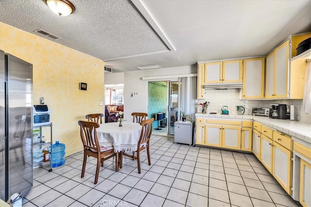 kitchen with light tile patterned floors, stainless steel fridge, backsplash, tile counters, and a textured ceiling