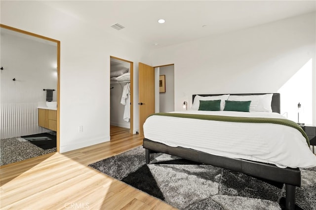 bedroom with ensuite bathroom, recessed lighting, wood finished floors, visible vents, and a walk in closet