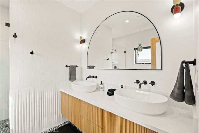 bathroom with a tile shower, double vanity, and a sink