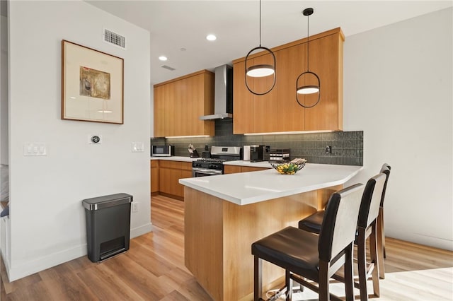 kitchen with a breakfast bar area, visible vents, appliances with stainless steel finishes, wall chimney range hood, and tasteful backsplash