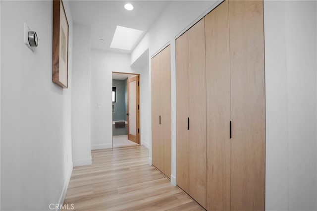 hallway featuring light wood-style floors, a skylight, and baseboards