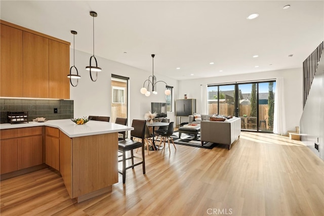 kitchen with light wood-style flooring, a peninsula, light countertops, backsplash, and a kitchen bar