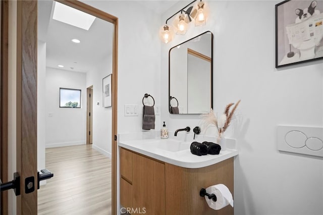 bathroom with a skylight, baseboards, wood finished floors, vanity, and recessed lighting