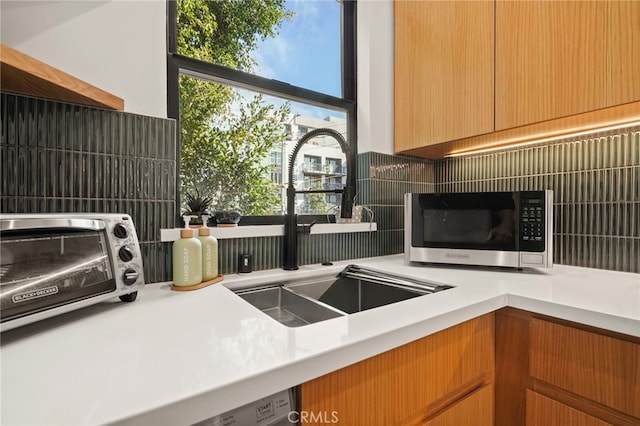 kitchen featuring light countertops, stainless steel microwave, a sink, and decorative backsplash