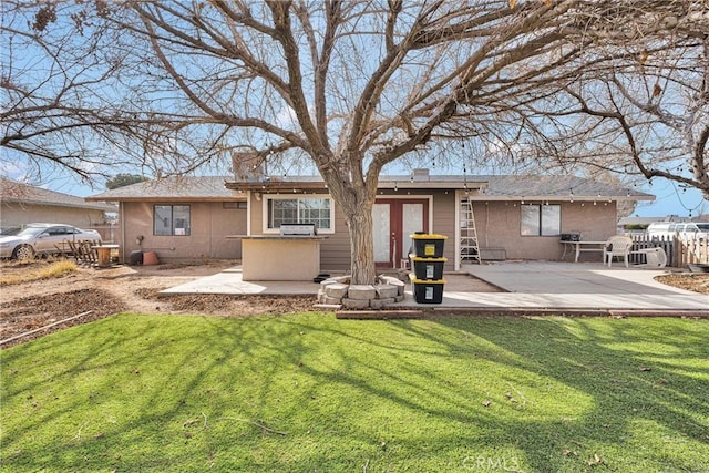 rear view of house featuring a patio area, a chimney, stucco siding, and a yard