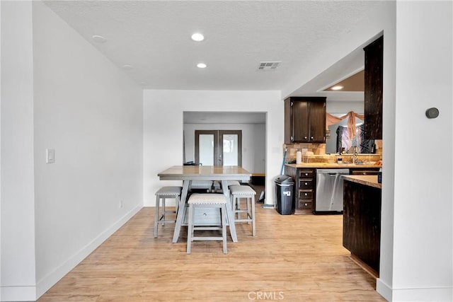 kitchen with light countertops, visible vents, light wood-style flooring, stainless steel dishwasher, and dark brown cabinets