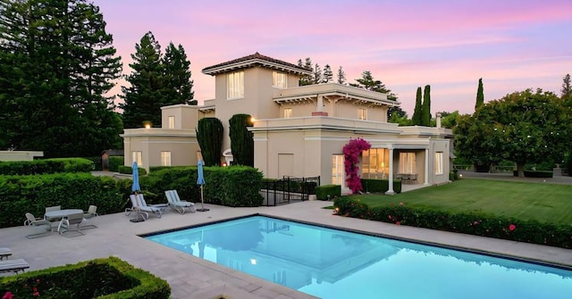 back house at dusk featuring a balcony, a yard, and a patio area