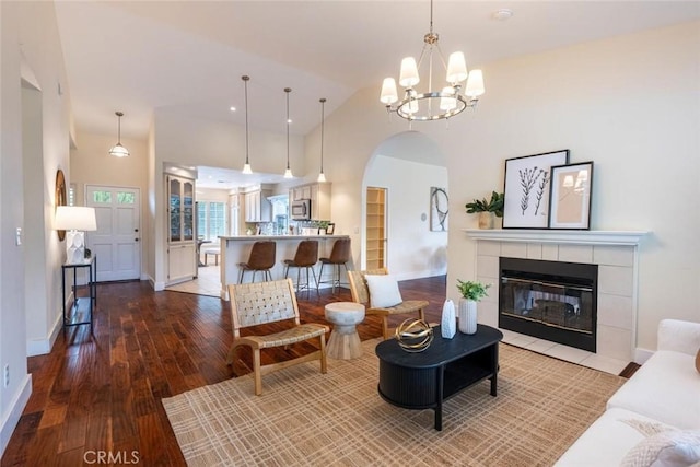 living room featuring wood-type flooring, high vaulted ceiling, a tile fireplace, and a notable chandelier