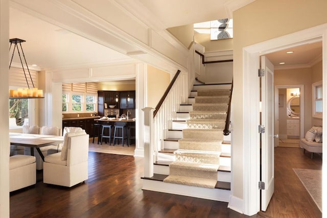 stairs featuring crown molding, wood-type flooring, and a chandelier