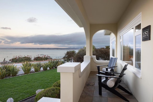 patio terrace at dusk featuring a yard and a water view