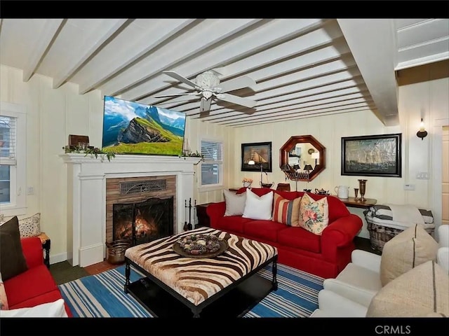 living room featuring ceiling fan, a premium fireplace, and beam ceiling