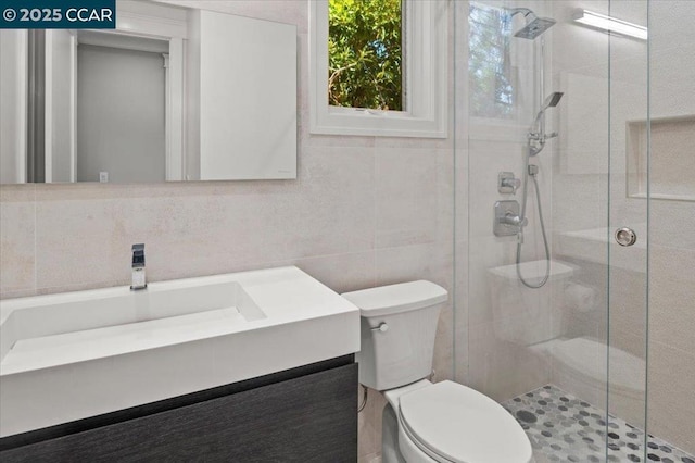 bathroom featuring vanity, toilet, a shower with door, and tile walls