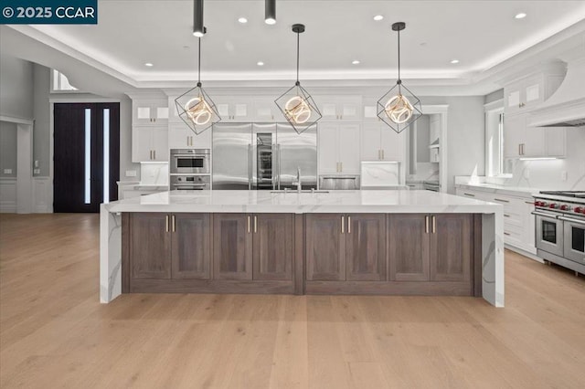 kitchen featuring a spacious island, high quality appliances, a raised ceiling, and white cabinets