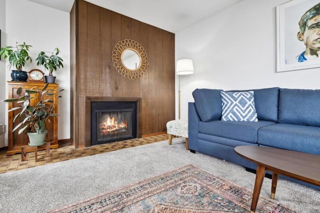 carpeted living room featuring a large fireplace and wooden walls