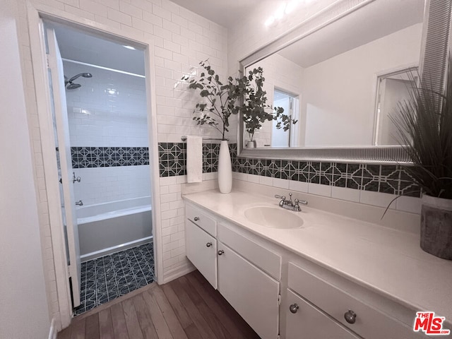 bathroom featuring tiled shower / bath, tasteful backsplash, tile walls, hardwood / wood-style flooring, and vanity