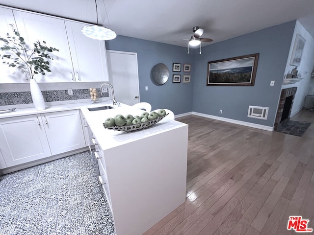 kitchen with sink, white cabinetry, wood-type flooring, a brick fireplace, and hanging light fixtures