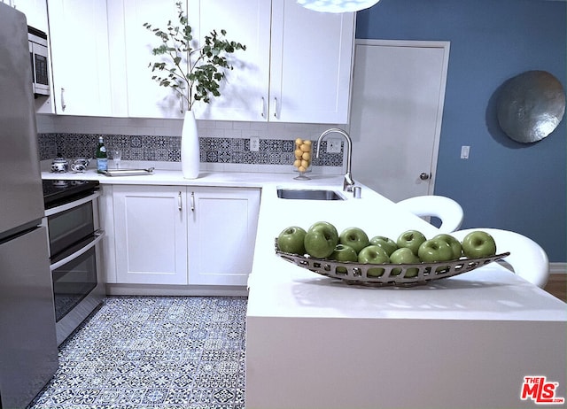 kitchen with sink, white cabinetry, light tile patterned floors, stainless steel appliances, and backsplash