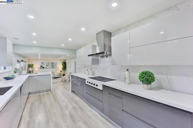 kitchen with white cooktop, tasteful backsplash, gray cabinets, light hardwood / wood-style floors, and wall chimney range hood