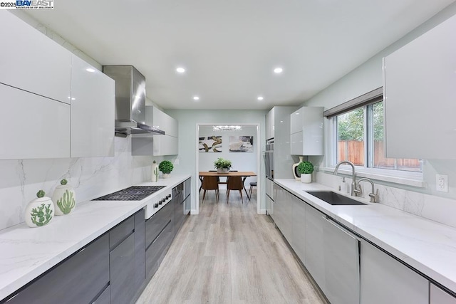 kitchen with wall chimney range hood, sink, white gas stovetop, light stone countertops, and white cabinets