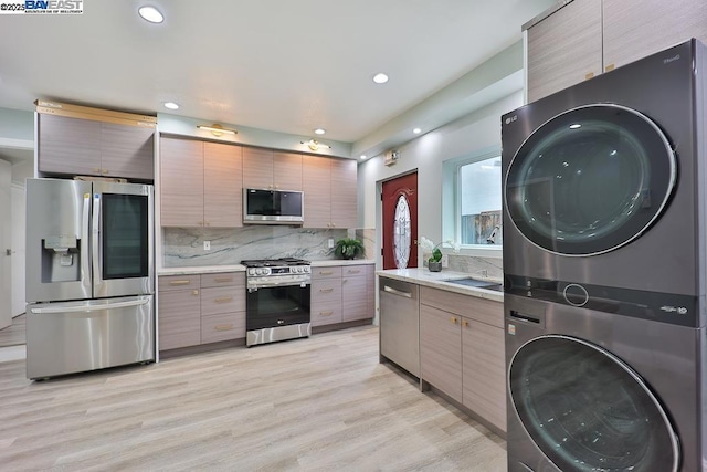 kitchen featuring sink, tasteful backsplash, appliances with stainless steel finishes, stacked washer / dryer, and light hardwood / wood-style floors