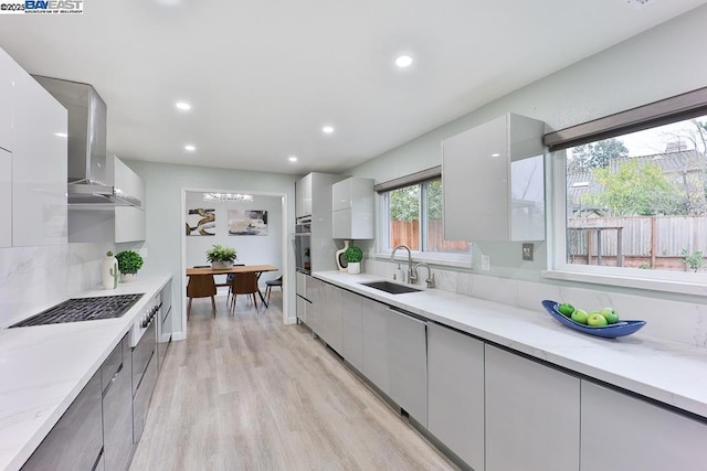 kitchen with sink, light stone counters, light hardwood / wood-style flooring, oven, and wall chimney range hood