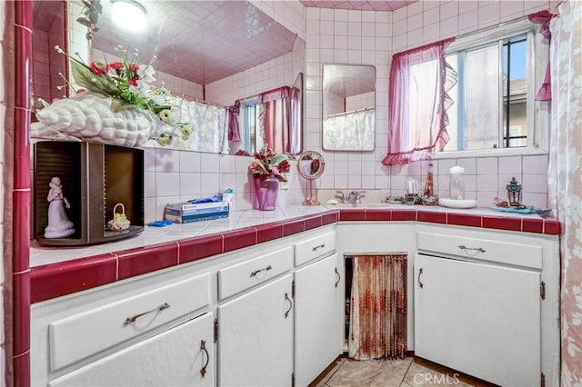 kitchen with sink, white cabinetry, backsplash, tile counters, and light tile patterned flooring