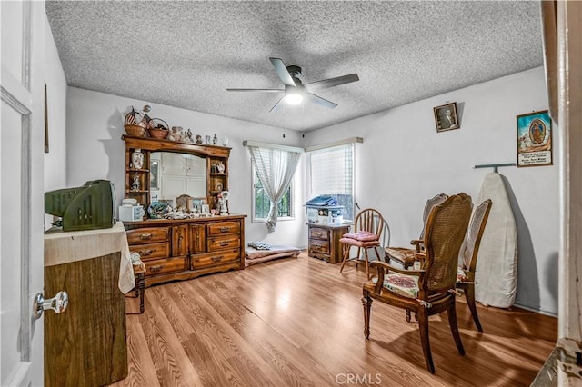 sitting room with ceiling fan, a textured ceiling, and light wood-type flooring