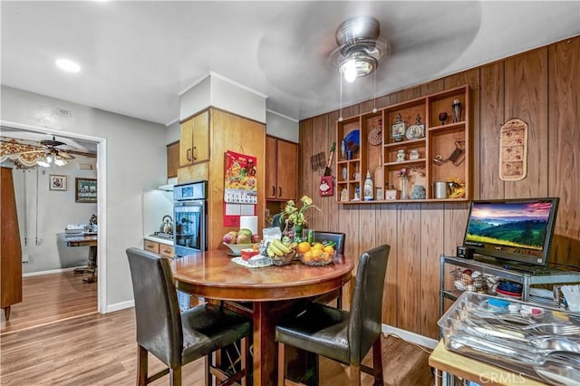 dining area featuring ceiling fan, light hardwood / wood-style flooring, and wood walls