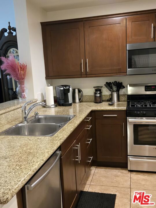 kitchen featuring light tile patterned flooring, appliances with stainless steel finishes, sink, light stone countertops, and dark brown cabinets