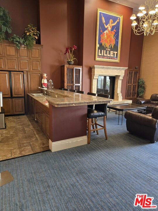 bar featuring a towering ceiling, pendant lighting, a fireplace, dark carpet, and light stone counters