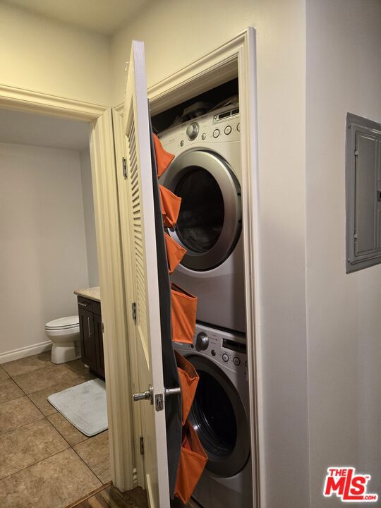 laundry area featuring stacked washer and dryer, electric panel, and light tile patterned flooring