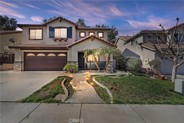 mediterranean / spanish home with a garage, driveway, a tiled roof, and stucco siding