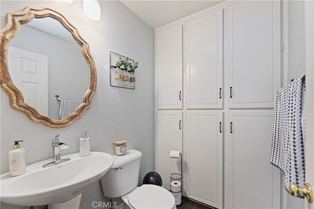 bathroom with a textured wall, a sink, and toilet