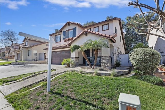 mediterranean / spanish home featuring driveway, stone siding, a tile roof, an attached garage, and a front lawn