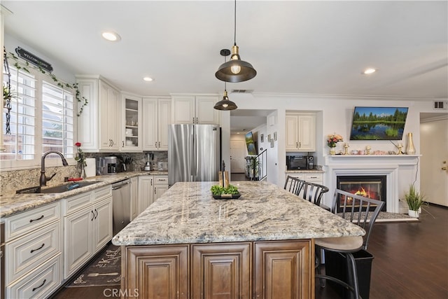 kitchen featuring light stone counters, visible vents, appliances with stainless steel finishes, a glass covered fireplace, and a sink