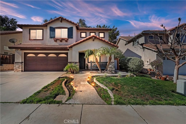 mediterranean / spanish-style house with a tile roof, stucco siding, concrete driveway, an attached garage, and stone siding